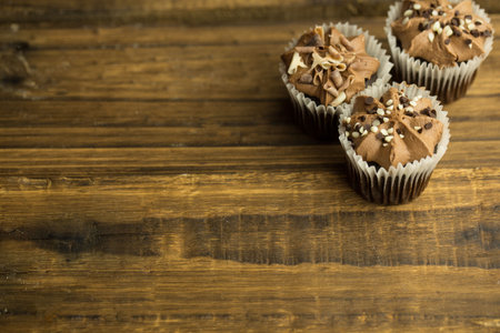 Three chocolate cupcakes are being shown in flat design on wooden tabletop, copy space. Bakery, dessert, confections, rustic, cozy, handcrafted, gourmetの写真素材