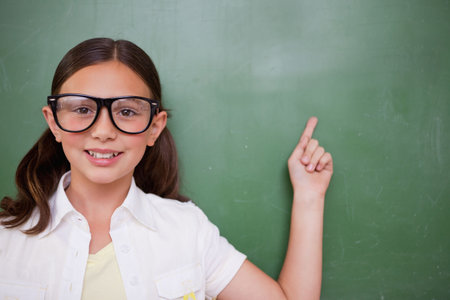 Flat design illustration is showing girl wearing glasses pointing at green chalkboard, copy space. Student, education, classroom, learning, teaching, presentation, curiosityの写真素材