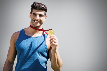 Portrait of happy sportsman showing medal against gray backgroundの写真素材
