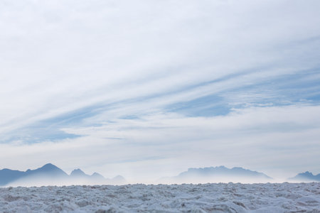 Flat design salt flat is stretching toward misty mountain ridge under wispy cloud layers. Minimalist, serenity, nature, landscape, atmospheric, vast, scenicの写真素材