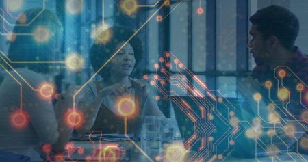 Discussing two colleagues collaborating over documents in office, with digital circuit graphics....