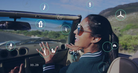 Talking woman in sweater gesturing in convertible car on rural road with data overlays, copy space. Automobile, travel, leisure, modern, technology, adventure, scenicの写真素材