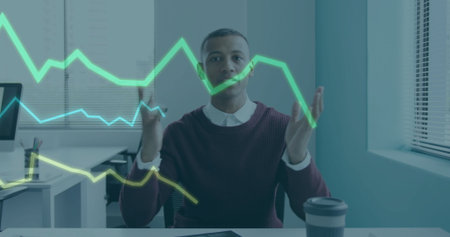 Gesturing male professional analyzing holographic line charts at office with laptop and coffee cup. Business, technology, innovation, data, futurism, productivity, corporateの写真素材