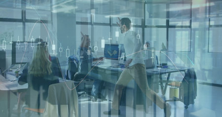 Gesturing employee in white shirt and khakis by laptops in open office with financial chart overlay....