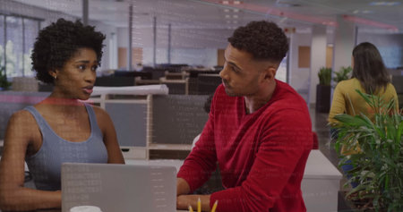 Discussing coworkers wearing casual tops exchanging ideas at open-plan office with silver laptop....