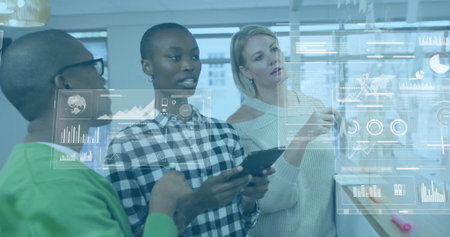 Analyzing co-workers reviewing translucent data projections on glass in modern office, with tablet. Collaboration, analytics, innovation, technology, teamwork, forecasting, modernityの写真素材