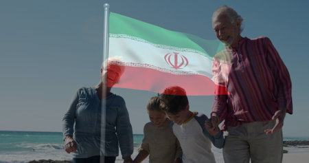 Walking grandparents and grandchildren holding hands along sandy beach, with fluttering flag. Heritage, multigenerational, outdoor, scenic, leisure, unity, tranquilityの写真素材