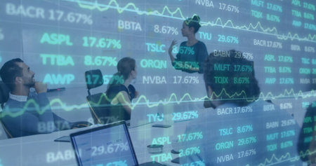 Presenting businesswoman pointing at financial charts on glass wall in meeting room, with laptops....