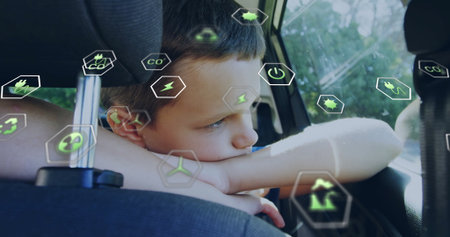 Leaning school-age boy gazing outside window in car back seat, with green energy icons....