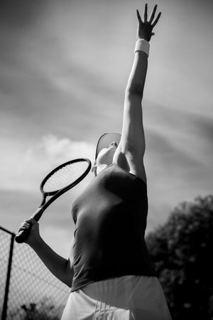 Low angle view of young woman serving tennis ball against skyの写真素材