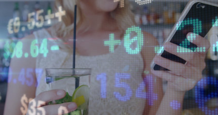Holding smartphone and sipping mint lime cocktail at bar counter, showing floating numeric overlays. Cocktail, technology, modern, nightlife, social, digital, leisureの写真素材