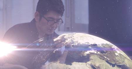 Leaning mature Asian man observing holographic Earth globe projection in office, with keyboard....