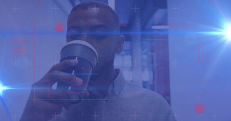 Sipping coffee from cup, man wearing blue shirt standing in office corridor with digital overlays....