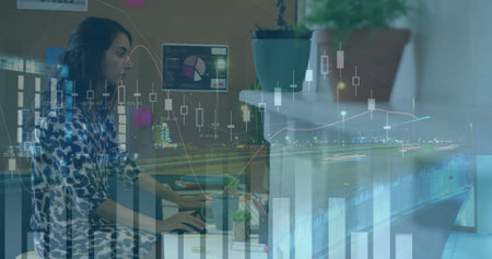 Typing female data analyst analyzing financial charts at office desk, including laptop and monitor....