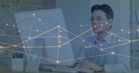 Typing senior Japanese man wearing blue shirt at office desk, with colored pencils, copy space. Professional, workspace, minimalist, creativity, focus, modern, productivityの写真素材