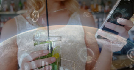 Woman wearing top interacting with smartphone and drinking green cocktail at bar, with HUD graphics. Luxury, technology, modern, social, vibrant, nightlife, chicの写真素材