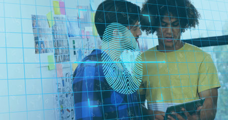 Two colleagues in blue and yellow shirts examining tablet with fingerprint grid overlay in office. Collaboration, innovation, modernity, technology, urban, teamwork, brainstormingの写真素材