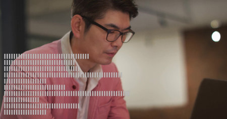 Focusing Asian man wearing pink blazer typing on laptop at modern office desk, with eyeglasses....