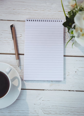 Close-up of spiral book and pen between coffee cup and flower pot on tableの写真素材