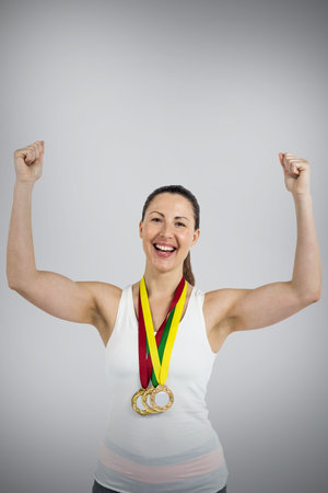 Portrait of female athlete with medals raising hands against gray backgroundの写真素材