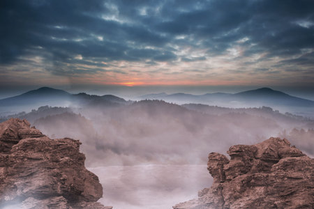 Mist filled mountain valley is being shown in flat design, featuring rugged cliffs and cloudy sky. Landscape, adventure, atmospheric, rugged, tranquility, scenic, naturalの写真素材