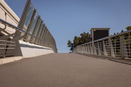 Flat design paved bridge deck rising toward top under clear sky with glass barriers metal railings. Urban architecture, modern infrastructure, public space, transportation, minimalism, outdoor environment, engineeringの写真素材