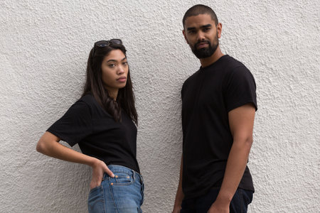 Flat design adult man and woman are leaning against stucco wall wearing black tees, jeans, shades. Casual, friendship, modern, lifestyle, urban, relaxed, youthfulの写真素材