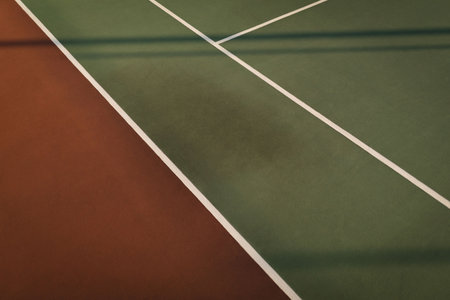 Flat-design court surface is showing brownish-red joining green with white lines and fence shadows. Sports, recreation, geometry, outdoor, athletic, minimalism, vibrantの写真素材
