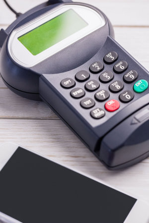 Showing payment terminal resting on wood tabletop in flat design, including smartphone edge....