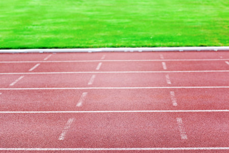 Flat design is showing red outdoor rubber track lanes with white markings leading into grass field. Athletics, stadium, sport, competition, fitness, outdoor, activeの写真素材