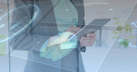 Holding tablet, executive in gray suit using holographic UI in office with grid charts plus icons....