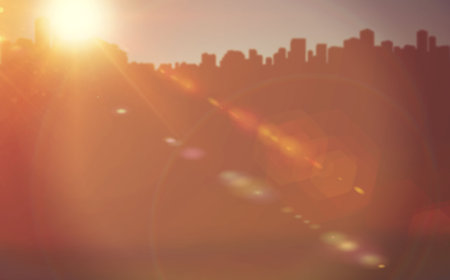 Flat design city skyline silhouette is spanning horizon during glowing orange-red sunset lens flare....