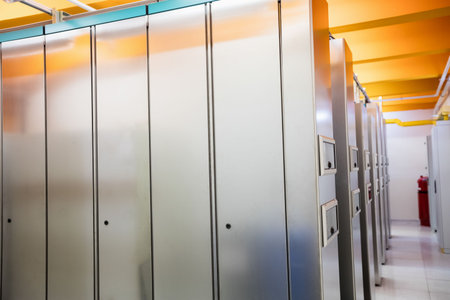 Row of tall grey cabinets is lining narrow corridor flat, with yellow ducts and red extinguisher....