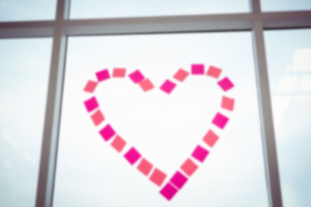 Low angle view of heart shape made from pink sticky notes on glass window against skyの写真素材