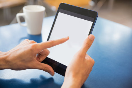 Cropped hand holding digital tablet by table at homeの写真素材