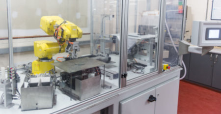 Flat design of yellow industrial robot arm is operating inside transparent enclosure on metal table....