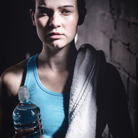 Portrait of confident young woman with bottle and towel standing at gym
