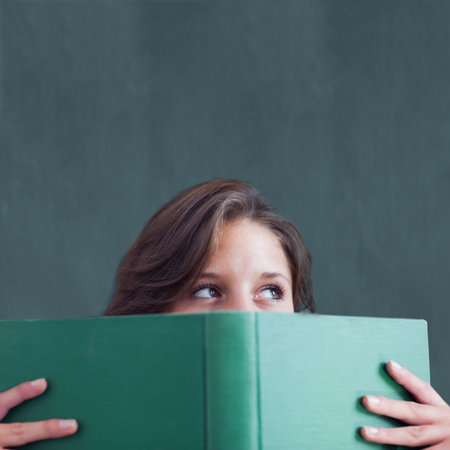 woman is holding green hardcover book while gazing right at dark green chalkboard in flat design. Literature, education, studious, intellectual, focused, classroom, contemplationの写真素材