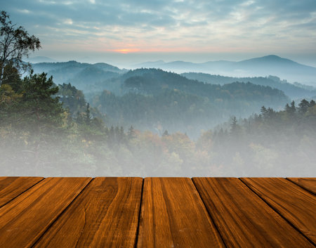 Wooden deck is being shown overlooking misty forested hills in flat design with soft sunrise glow. Nature, landscape, serenity, outdoors, wilderness, tranquility, scenicの写真素材