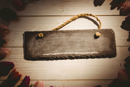 Flat design slate sign with frayed rope handle is lying on whitewashed planks with tulip border....