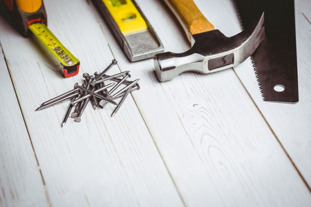 Flat design is showing tape measure, nails, spirit level, hammer, saw blade on white painted plank....