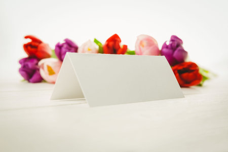 Flat design is featuring blank tent card on white tabletop with blurred red purple pink tulips. Minimalist, elegance, floral, invitation, studio, decor, soft lightingの写真素材