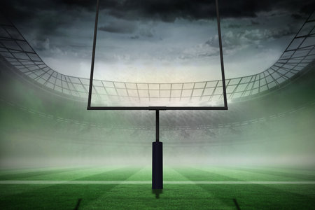 American football goal post is standing on green striped turf in misty stadium under overcast sky....
