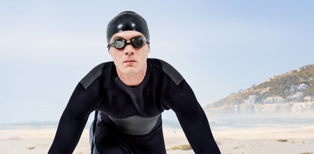 Portrait of male swimmer kneeling at beach against skyの写真素材