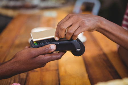 Close-up of woman paying bill through smartphone using NFC technology in cafeの写真素材
