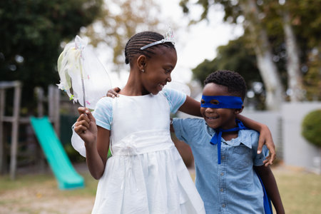 African american siblings wearing angel and superman costumes smiling and standing in park. Unaltered, love, together, childhood, happy and imagination concept.の写真素材