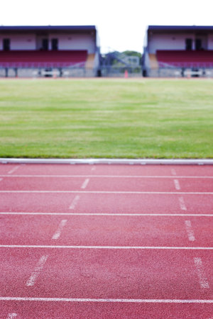 Flat design showing red running track lanes filling frame, white lane markers, grass field, stands. Athletics, sports, outdoor, arena, competition, fitness, enduranceの写真素材