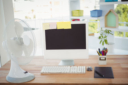 Electric table fan by computer with sticky notes on desk in officeの写真素材