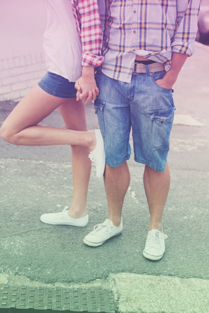 Low section of caucasian couple wearing white shoes and holding hands while standing on street. Unaltered, love, togetherness, fashion, shorts and lifestyle concept.の写真素材
