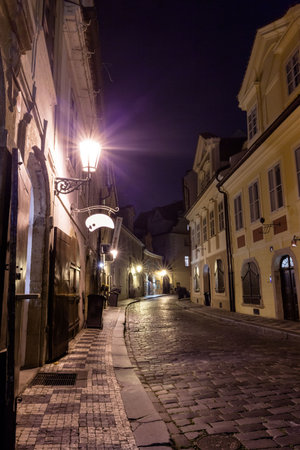 Flat style cobblestone street is glowing at night, featuring lanterns, shutters and signage bracket. Historic, romantic, vintage, atmospheric, architecture, nighttime, strollの写真素材